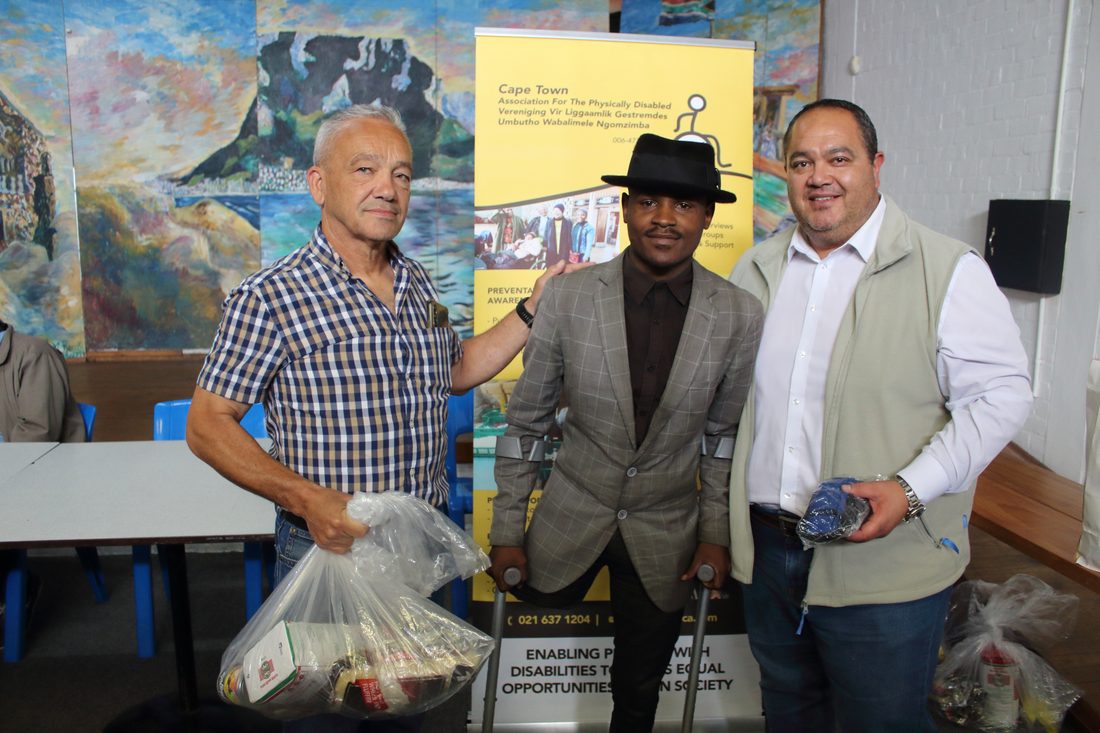 A Cape Town APD staff member handing a relief parcel to a smiling member in a wheelchair at a community handover